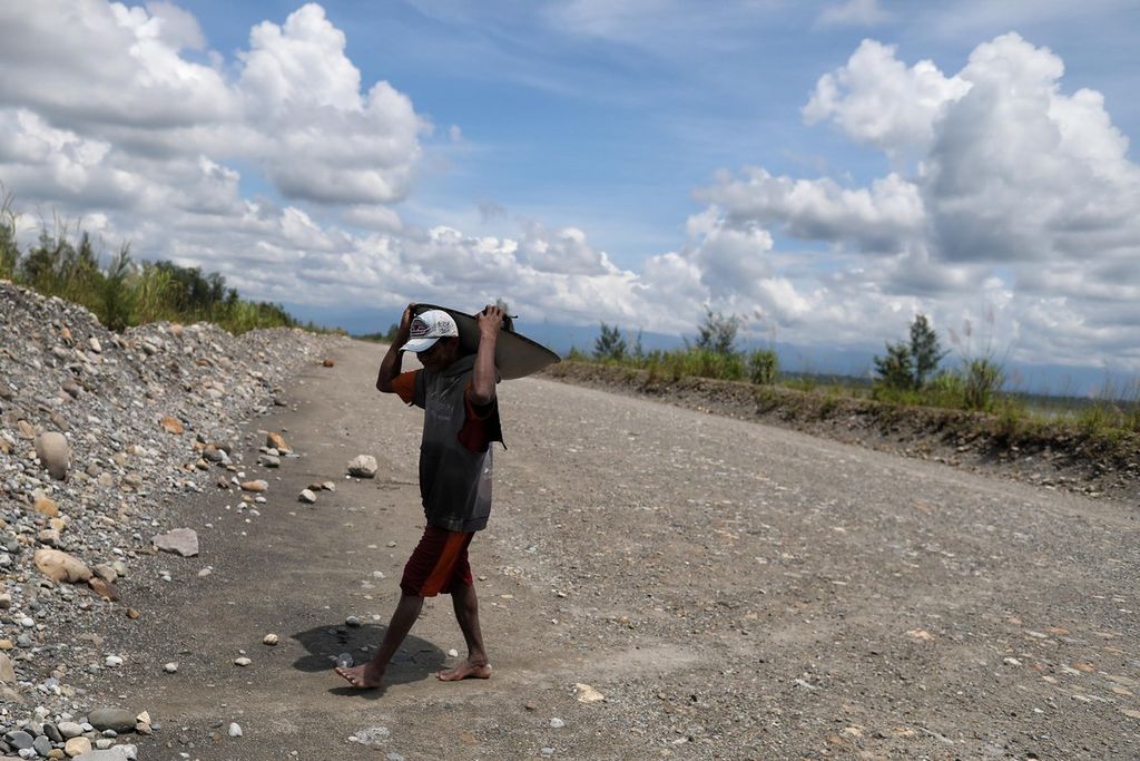 Elin Walten crosses an embankment while carrying a frying pan filled with fine sand at their camp inside PT Freeport Indonesia’s tailing deposition area on the Ajkwa River, Timika, Papua on Tuesday (26/10/2021)