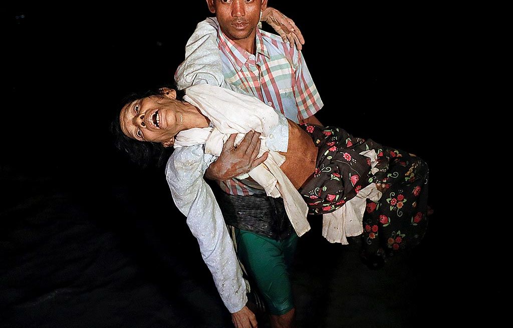 Nobi Hossain, warga Rohingya, menggendong kerabatnya saat bersama ratusan pengungsi Rohingya lain turun dari kapal kayu yang membawa mereka dari Myanmar ke  pesisir Shah Porir Dwip di Teknaf, dekat Cox\'s Bazar, Banglades, Rabu (27/9) malam.
