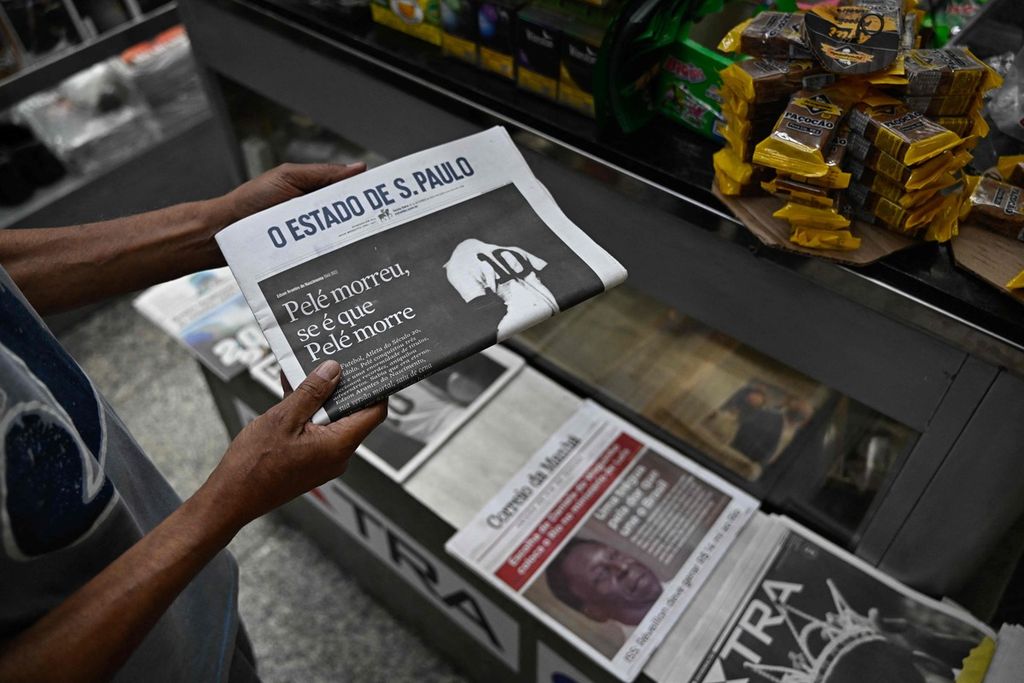 Seorangw arga memegang surat kabar dengan tajuk utama wafatnya legenda sepak bola Brasil Pele di kios surat kabar di Rio de Janeiro, Brasil, Jumat (30/12/2022). 