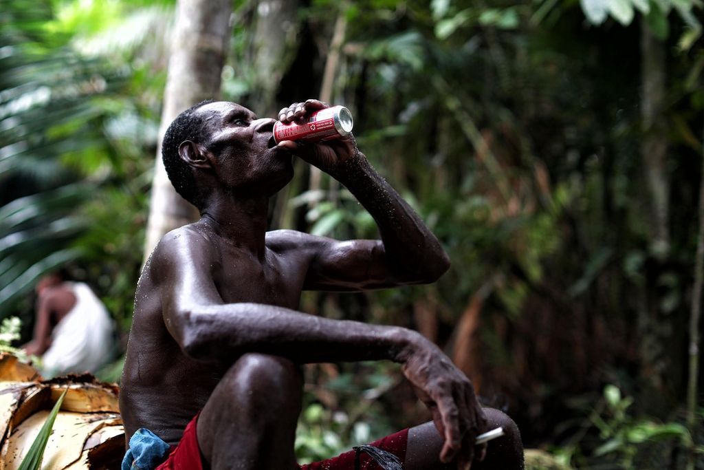 Abrham Jip menenggak minuman kaleng bersoda saat bersama warga kampung As dan Atat, Distrik Pulau Tiga, Asmat, Papua, memangkur sagu di hutan adat mereka, Kamis (14/10/2021).