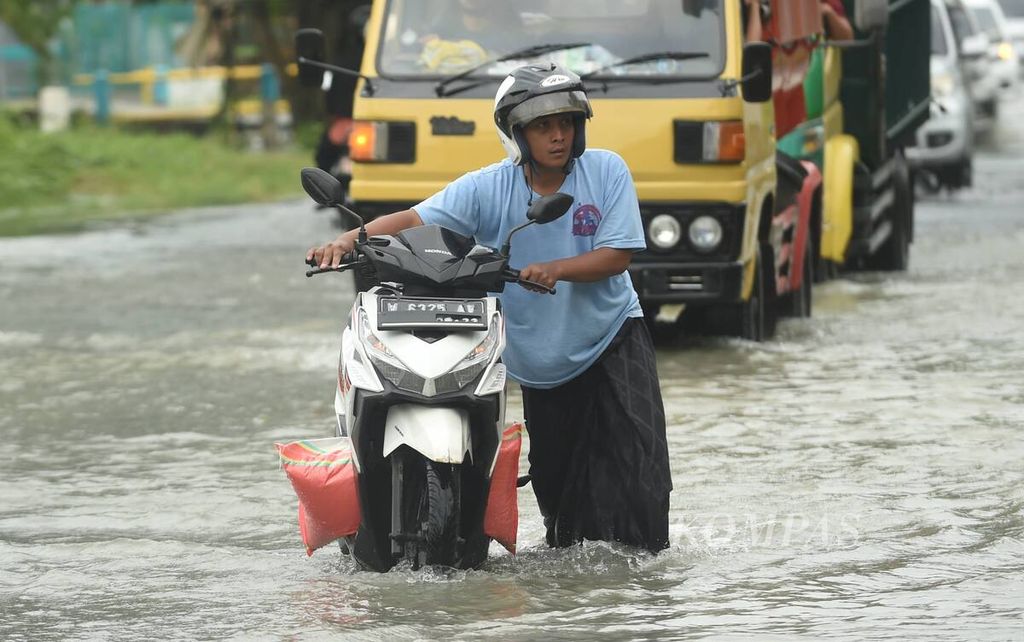 Pengendara mendorong sepeda motornya yang mogok akibat banjir di Jalan Raya Benjeng-Balonggpanggang, Kabupaten Gresik, Jatim, Jumat (11/2/2022).