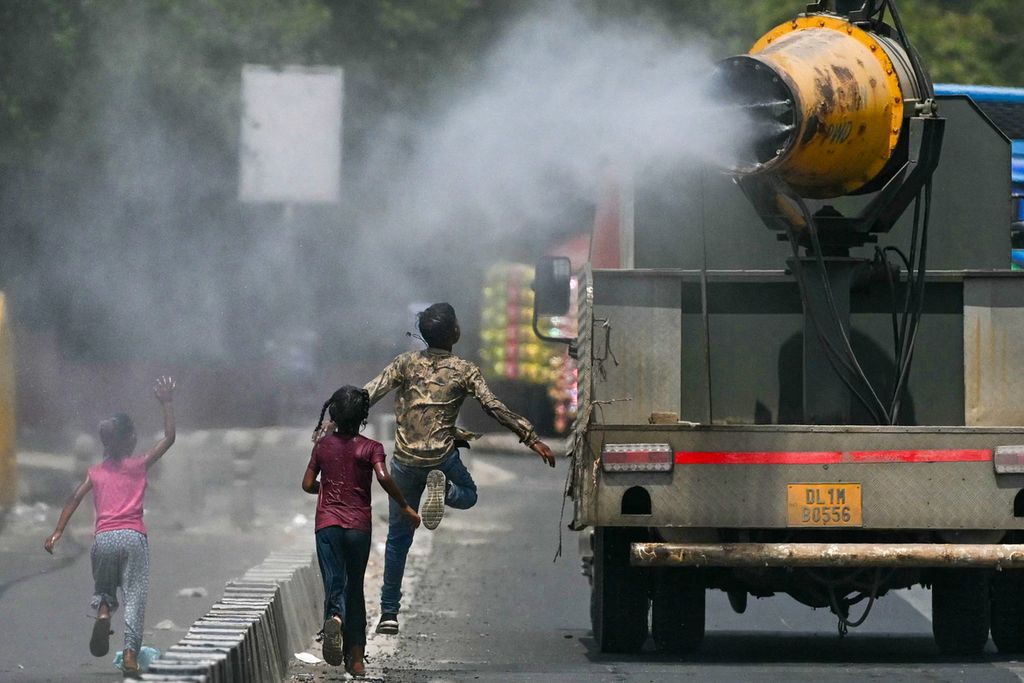 Anak-anak berlari di belakang truk penyemprot air di jalanan yang panas di New Delhi, India, 28 Met 2024. 