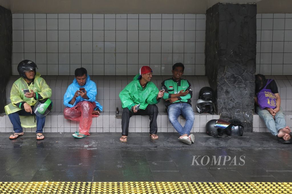 Pengendara ojek daring mengenakan jas hujan saat menunggu penumpang di kawasan Jalan MH Thamrin, Jakarta, Senin (29/1/2024). 