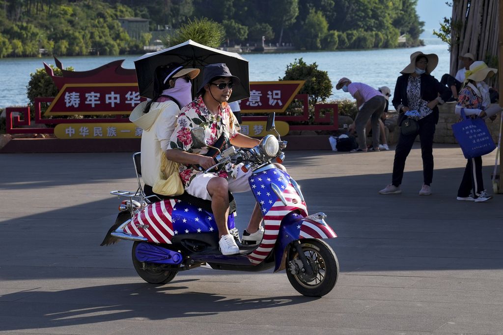 Pasangan anak muda mengendarai skuter berbendera AS di Dali, Provinsi Yunnan, China, 27 Juli 2022. 
