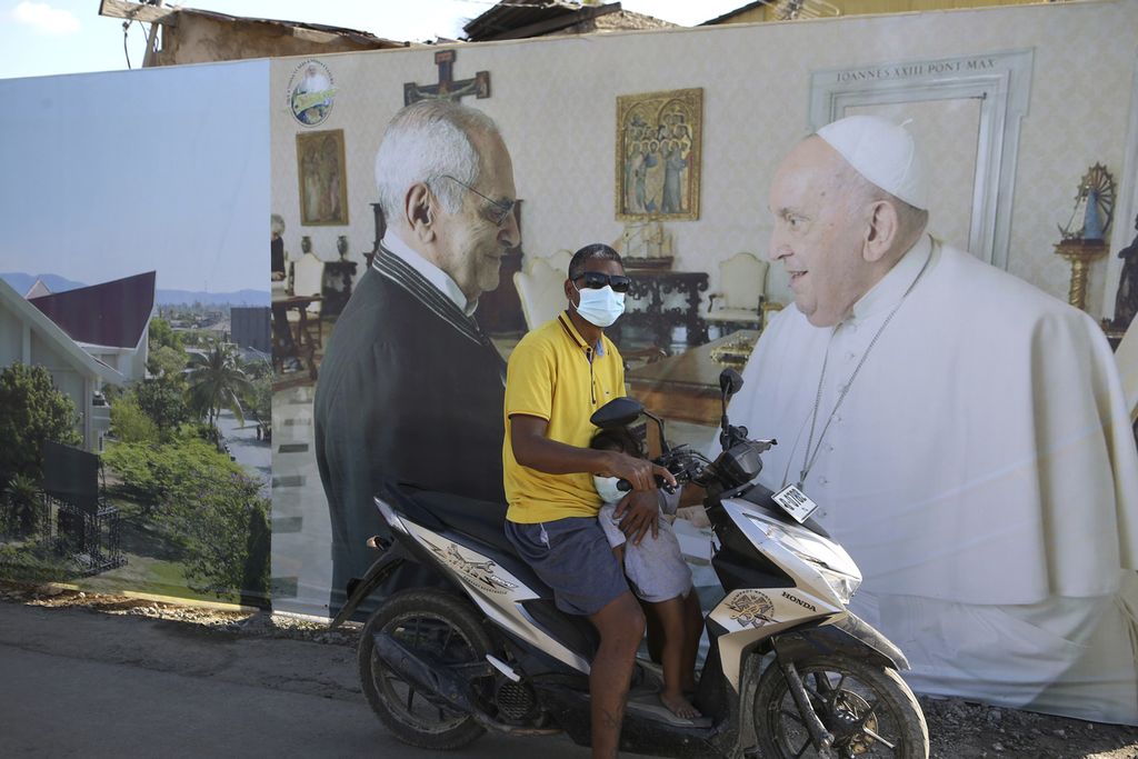 Seorang pria duduk di atas sepeda motornya di depan papan bergambar foto Paus Fransiskus untuk menyambut kedatangan Paus Fransiskus di Dili, Timor Leste, Selasa (3/9/2024). 