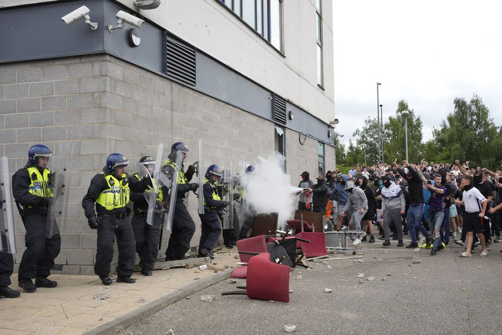  Seorang pengunjuk rasa mengarahkan alat pemadam kebakaran ke polisi yang berjaga dalam untuk rasa di luar hotel Holiday Inn Express di Rotherham, Inggris, Minggu (4/8/2024). 