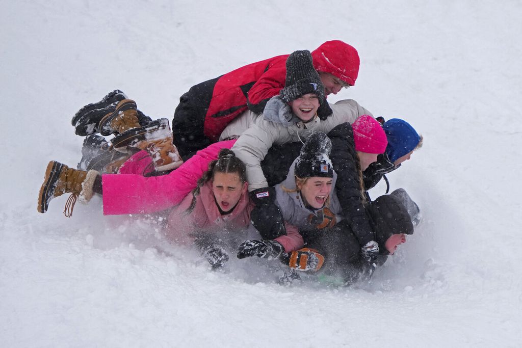 Anak-anak dan remaja bermain menuruni bukit bersalju di Provo, Utah, Rabu (22/2/2023). Badai musim dingin melanda Amerika Serikat dengan salju tebal hingga menghentikan penerbangan dan mematikan jaringan listrik.  