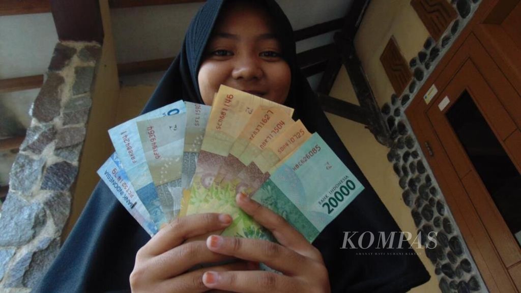 Pekerja tersenyum menunjukkan uang THR yang didapatkan saat Lebaran, Jumat (15/6/2018), di Kabupaten Indramayu, Jawa Barat.