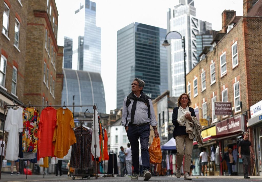 Para pejalan kaki berjalan melintasi pasar kaget Petticoat Lane Market dengan latar belakang The City, distrik keuangan di London, Jumat (11/8/2023).